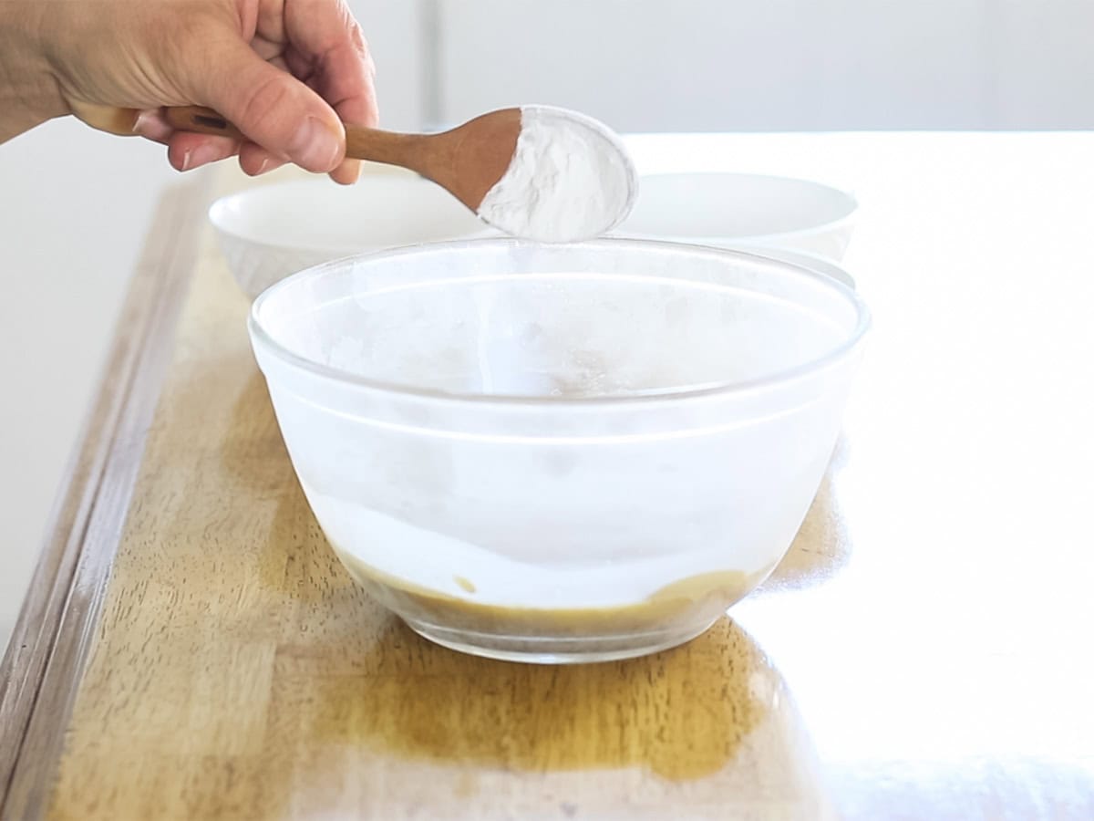 Adding a spoonful of arrowroot powder to the bowl of homemade body butter.
