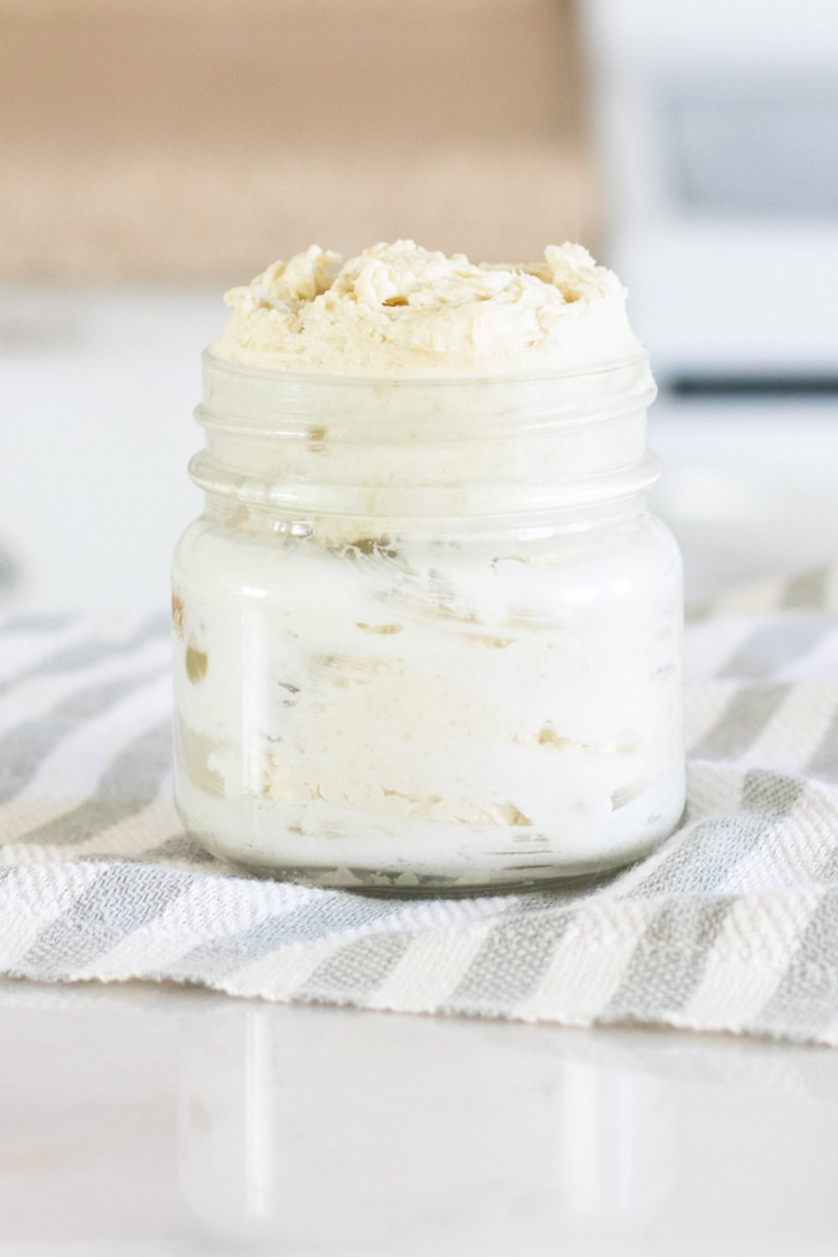A glass jar filled with homemade body butter sitting on a striped towel.