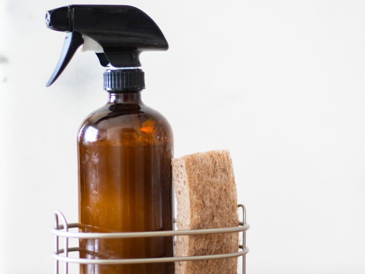 An amber bottle of homemade granite cleaner in a wire basket with a sponge.