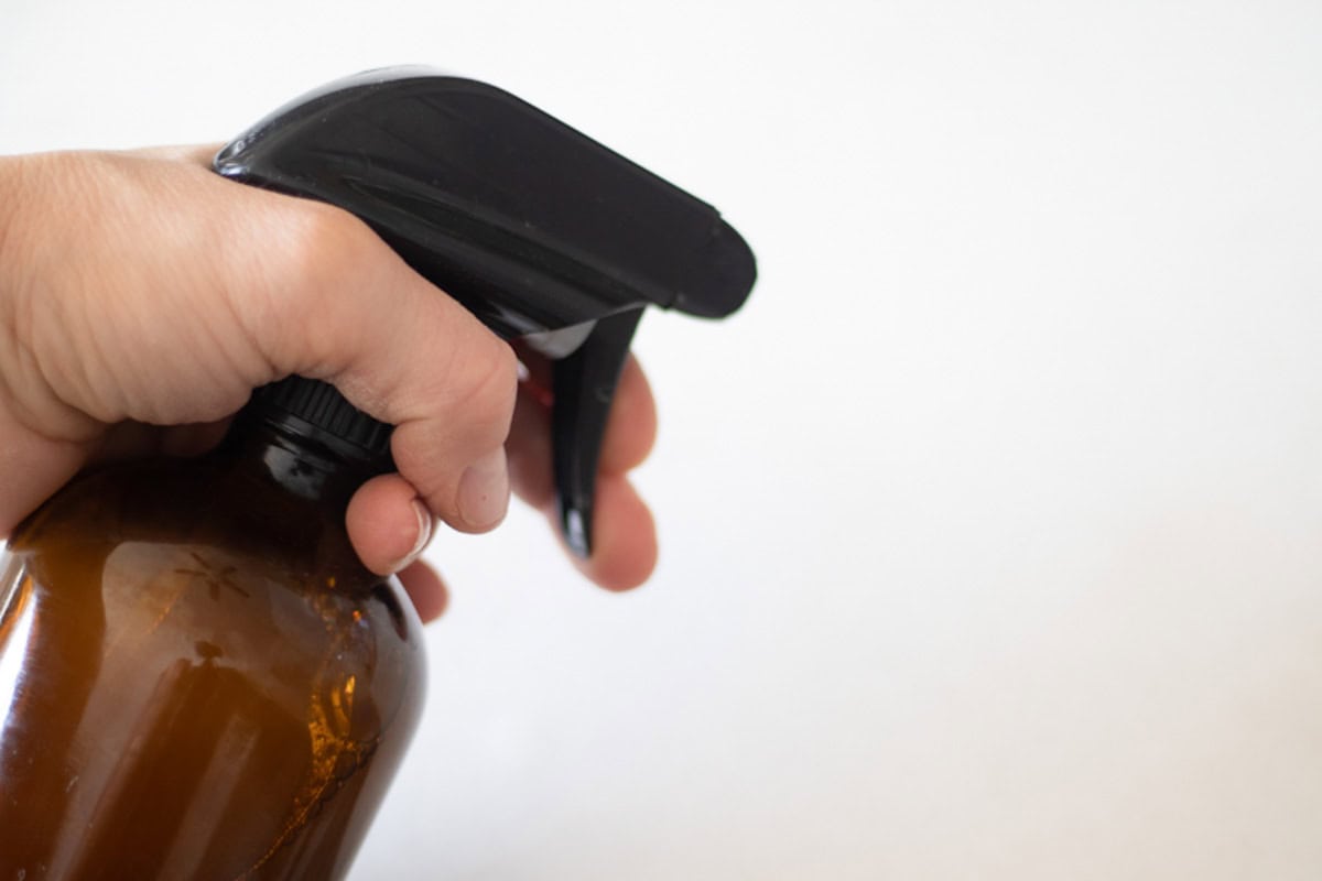 Spraying an amber glass spray bottle filled with homemade granite cleaner.