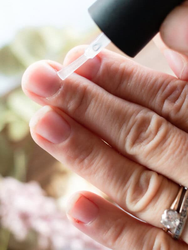 Brushing cuticle oil onto cuticles with a nail polish brush.
