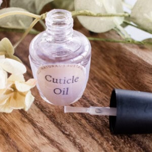 A bottle of cuticle oil on a wooden board with the nail brush sitting next to it.