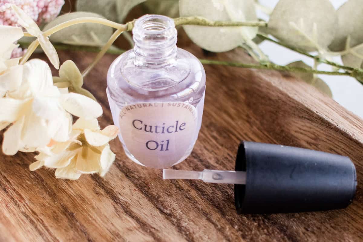 A bottle of cuticle oil on a wooden board with the nail brush sitting next to it.