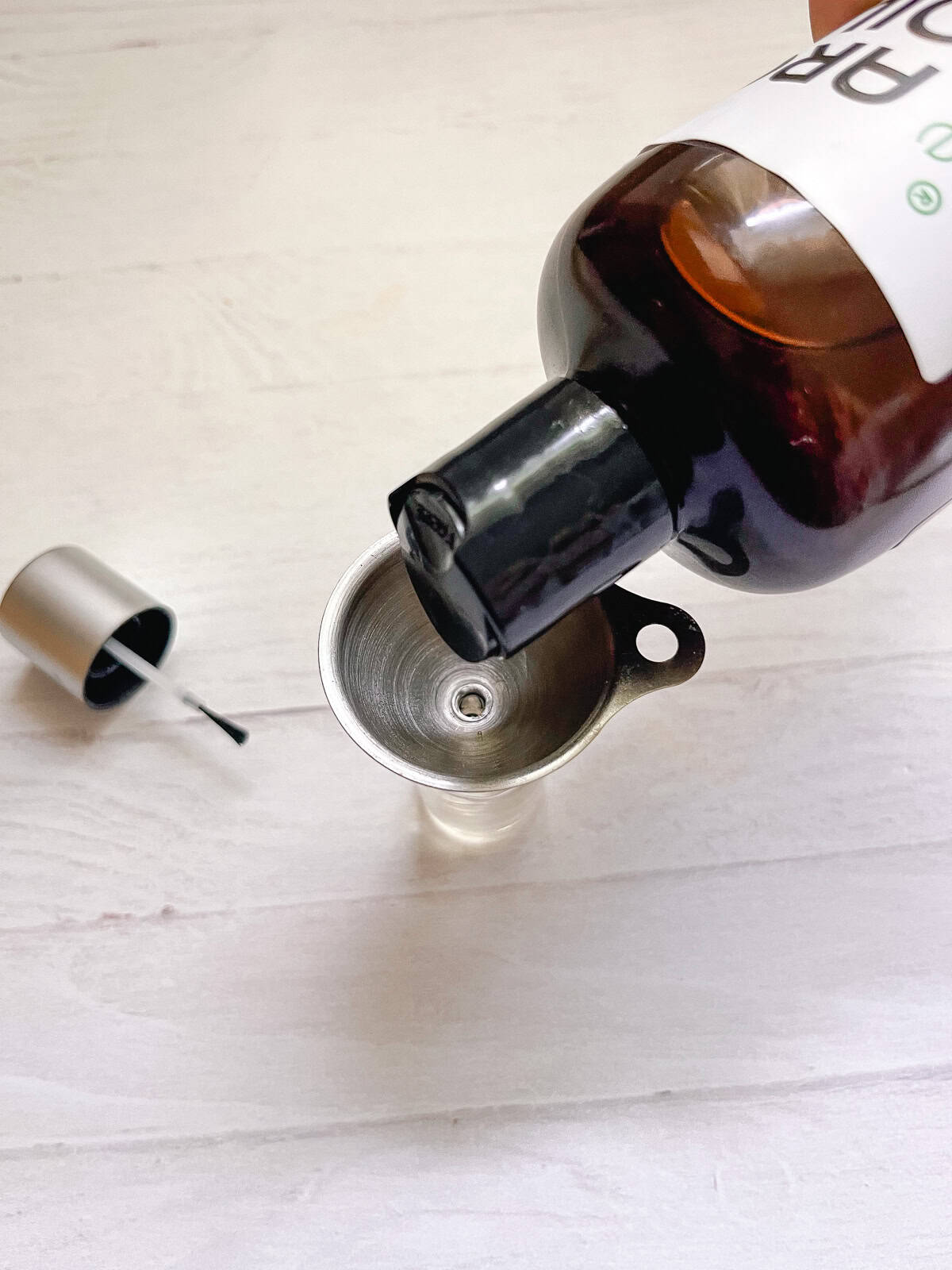 Pouring oil into an empty nail polish bottle with a small funnel. 
