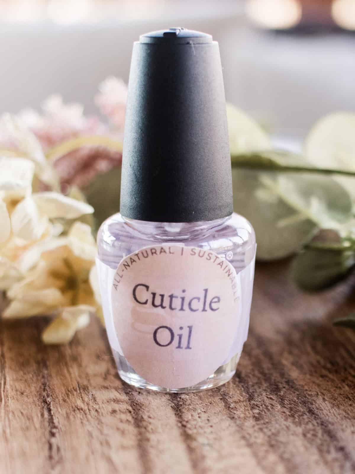 A bottle of homemade cuticle oil labeled with dried flowers behind it.