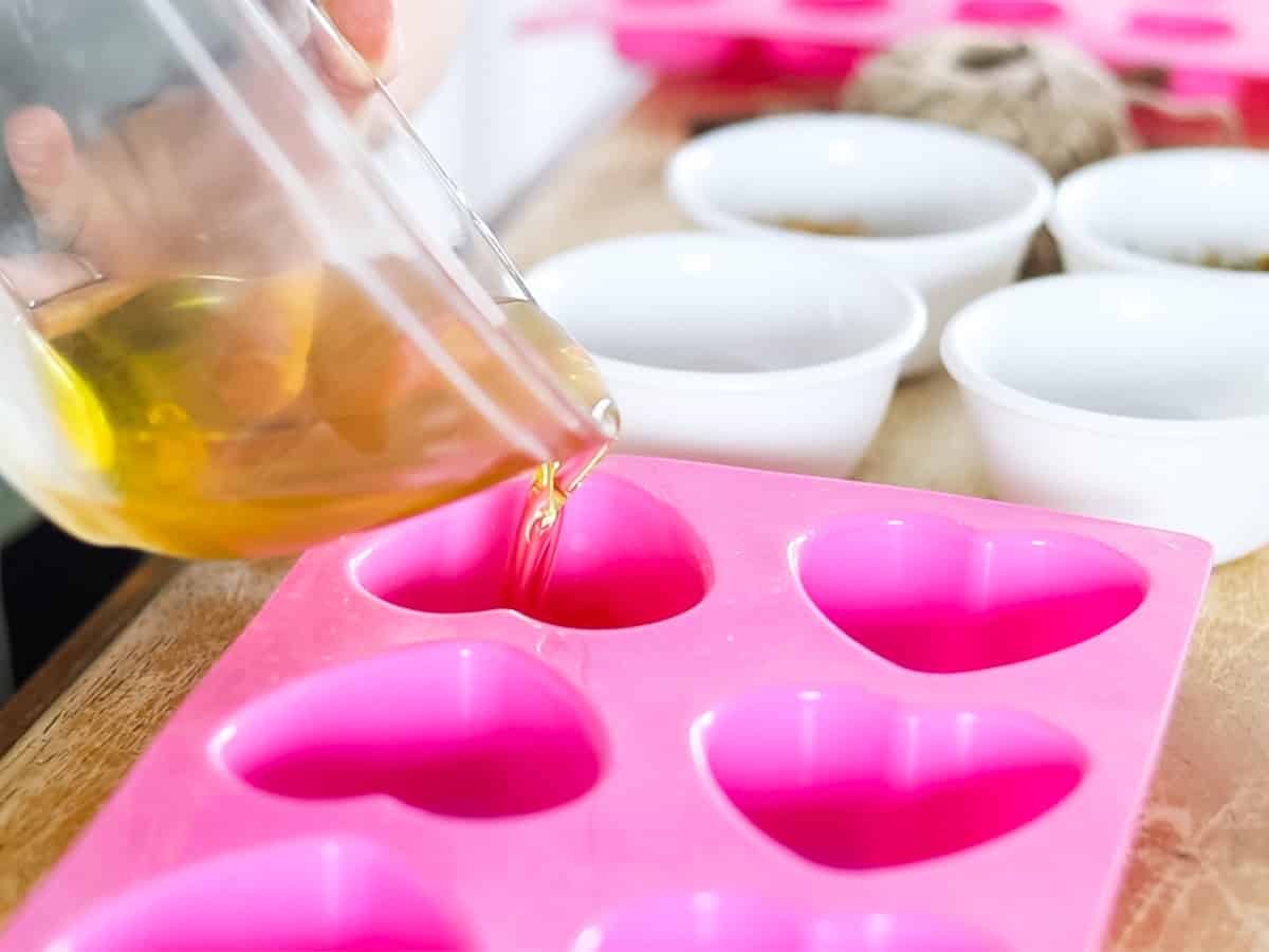 Pouring melted wax mixture into heart-shaped silicone molds. 