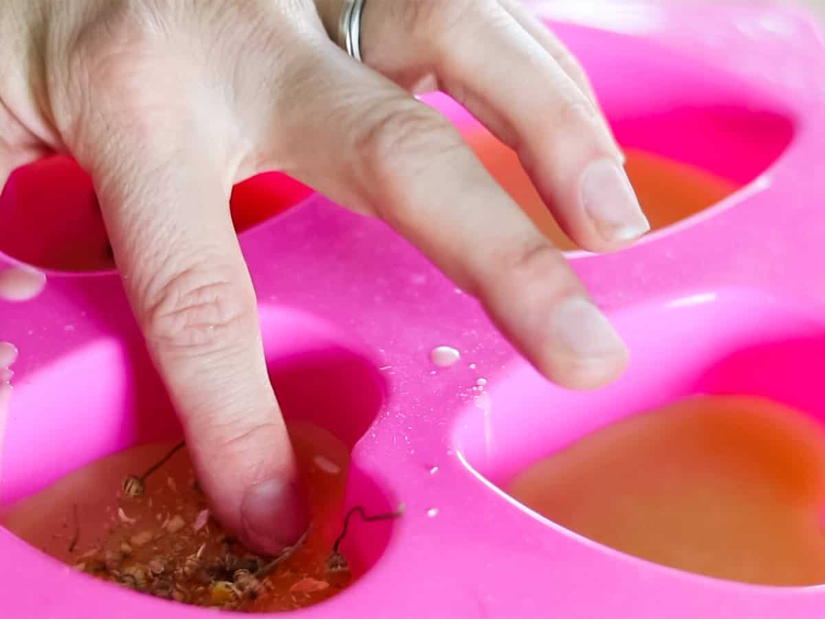 Adding dried flowers and herbs to silicone molds with melted wax in them.