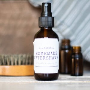 A bottle of homemade aftershave with a beard brush and essential oil bottles.