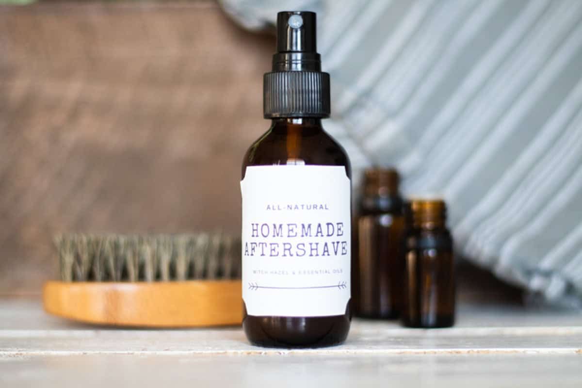 A bottle of homemade aftershave with a beard brush and essential oil bottles.