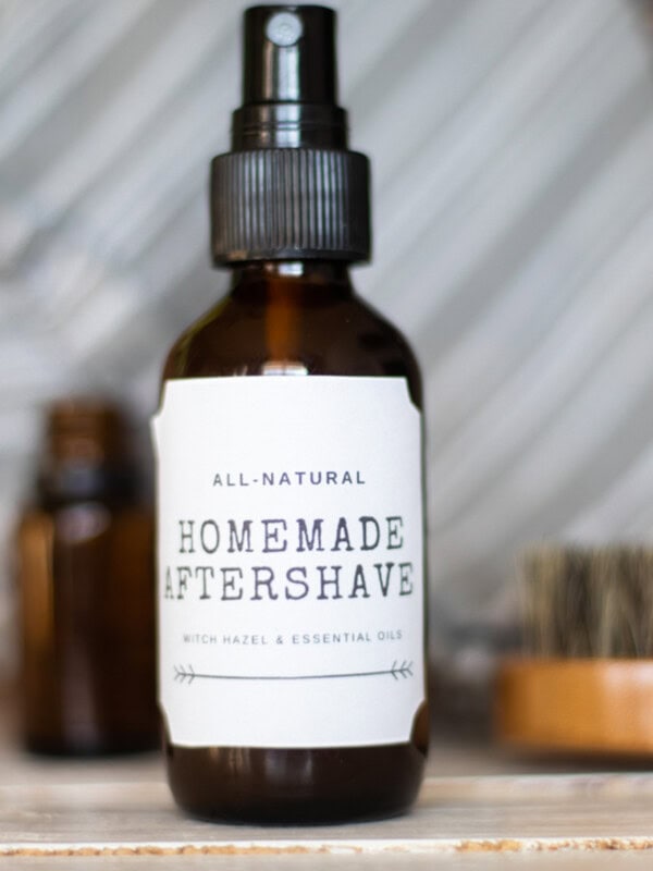A bottle of homemade aftershave with a printed label next to a brush and bottles of essential oils.