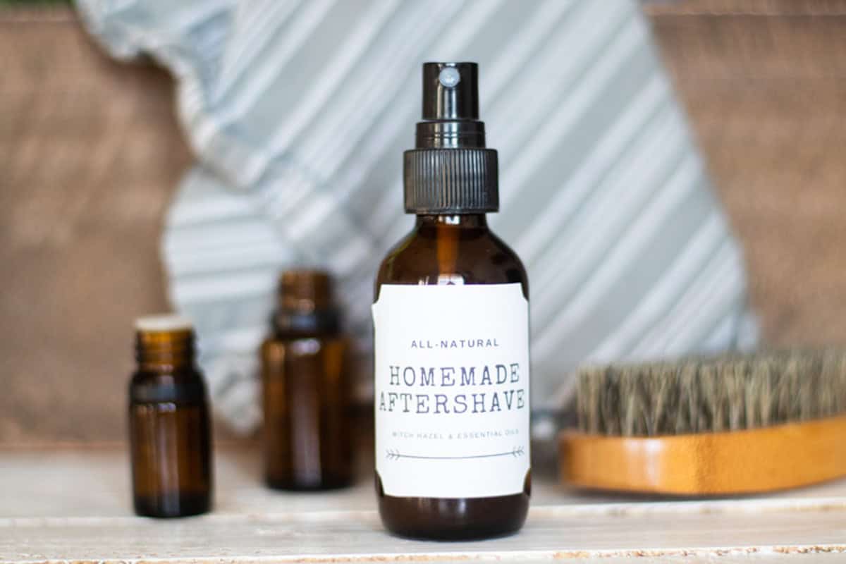 A bottle of homemade aftershave with a blue towel behind it and a brush next to it.