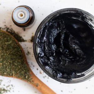 A bowl of drawing salve with a bottle of essential oil and a tablespoon of dried herbs.