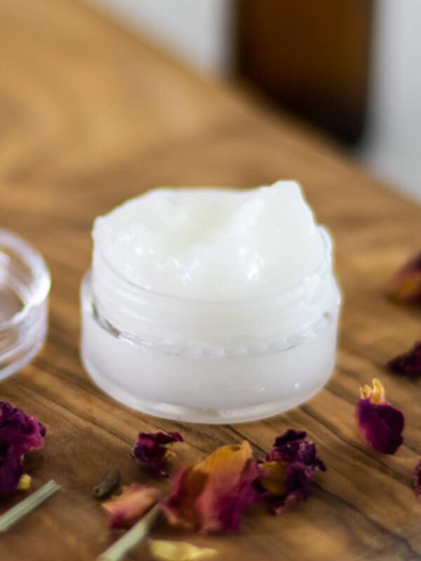 A small jar of homemade eye cream with dried flower petals around it.