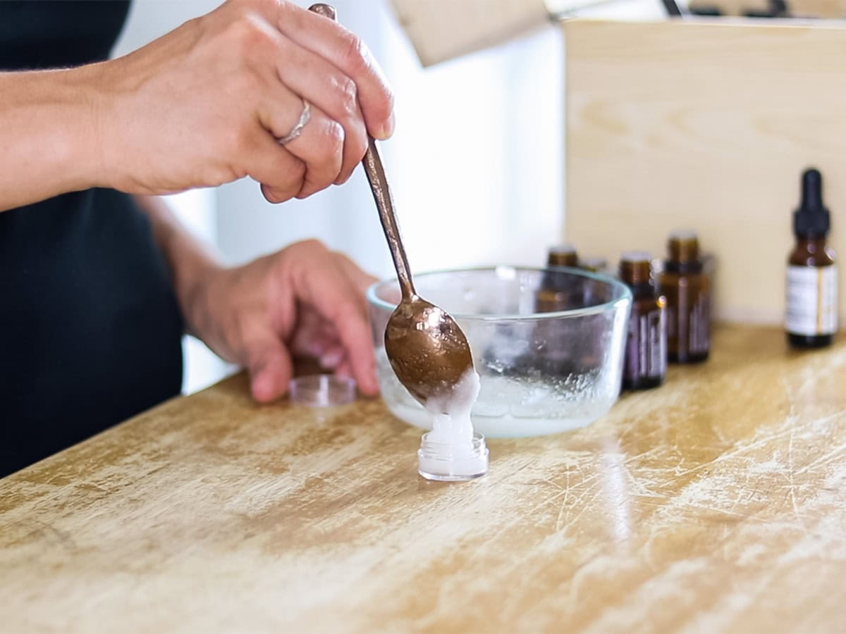 Scooping homemade eye cream into a small container with a spoon.