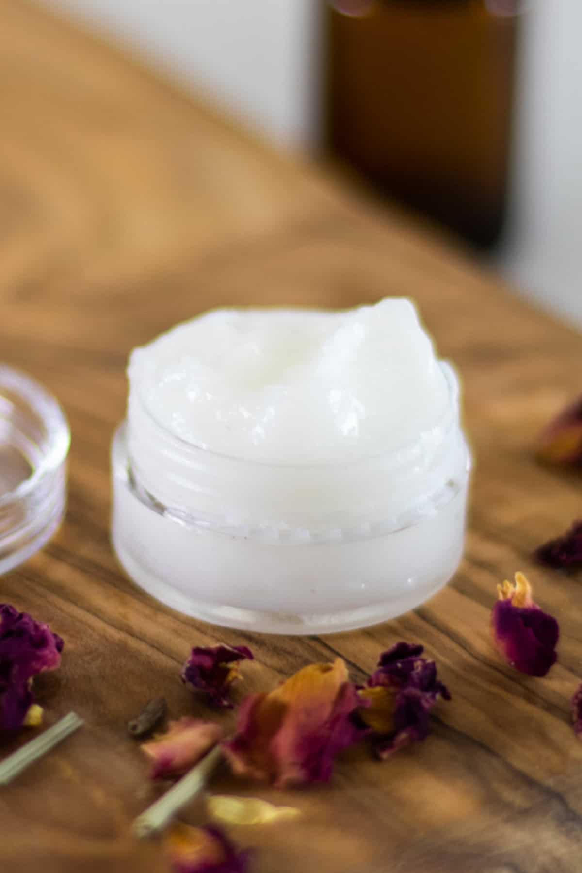 A small jar of homemade eye cream with dried flower petals around it.