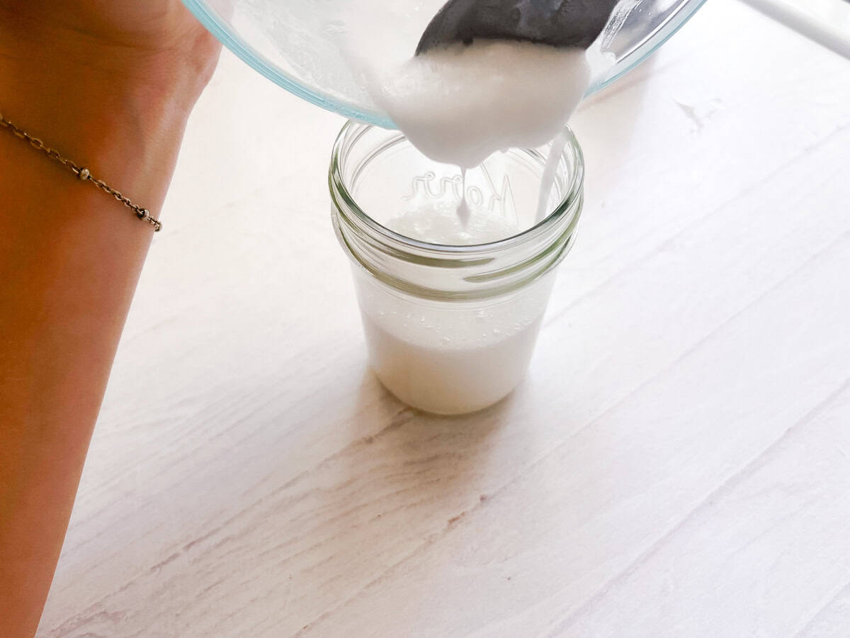 Pouring bathtub cleaner into a small glass jar. 
