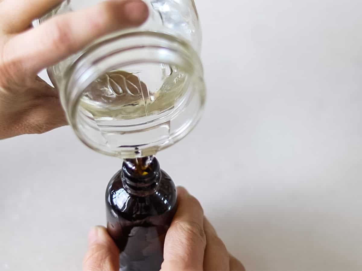 Pouring rubbing alcohol into a glass spray bottle out of a jar.
