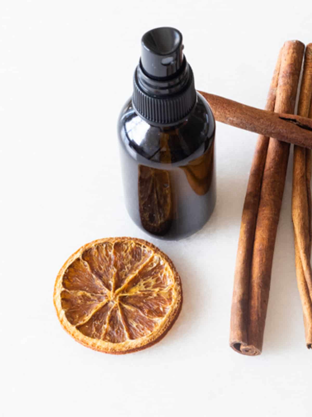 An amber spray bottle with cinnamon sticks and a dried orange slice.