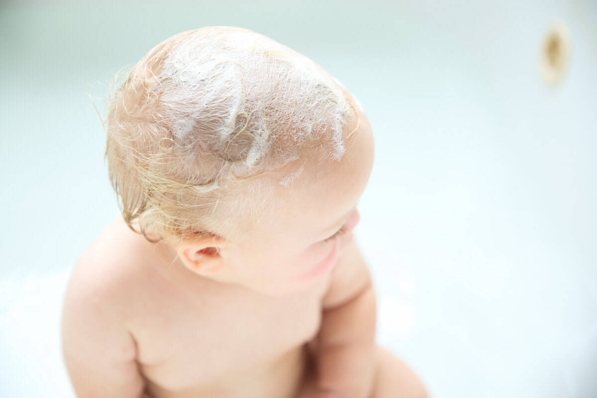 A baby with sudsy hair in the bathtub.