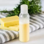 A bottle of homemade rosemary shampoo with a striped towel and soap bars.