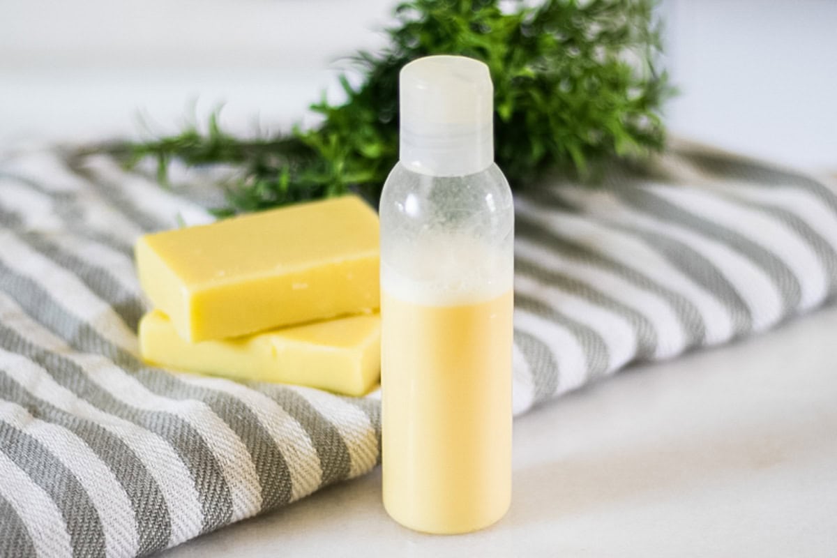 A bottle of homemade rosemary shampoo with a striped towel and soap bars.