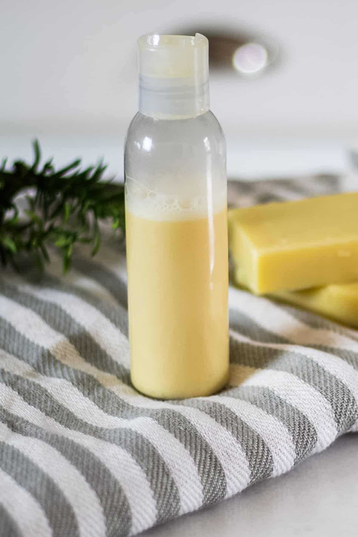 A bottle of homemade rosemary shampoo with a striped towel and soap bars.