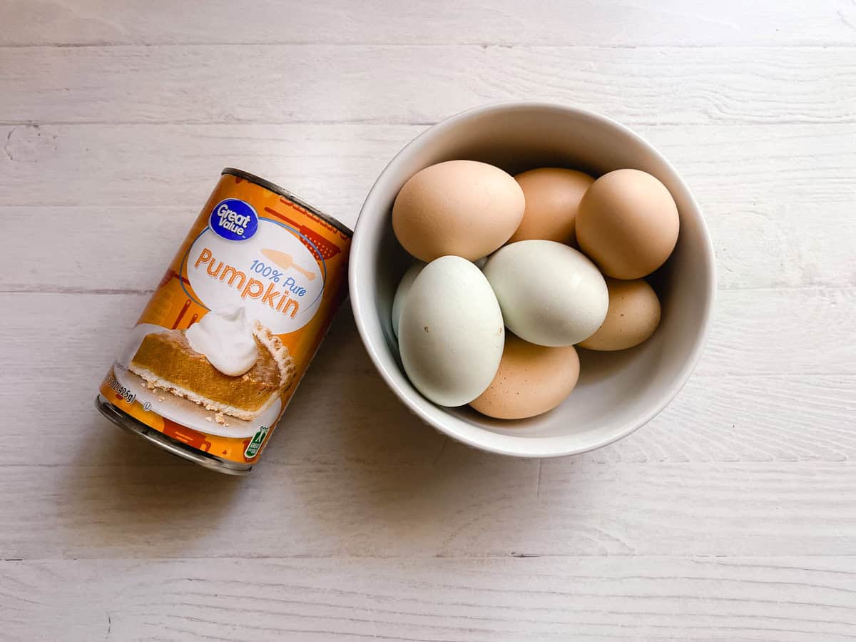 Healthy pumpkin pancake ingredients - a can of pumpkin and a bowl of eggs - on a white table.