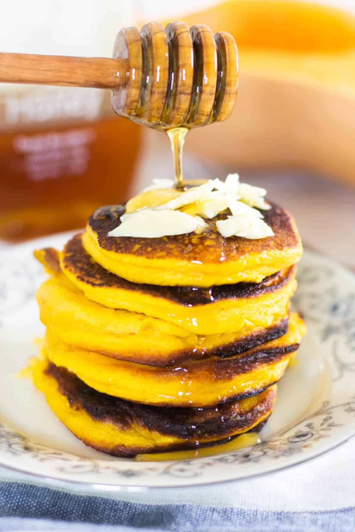 Healthy pumpkin pancakes in a stack with a honey dipper drizzling over them.