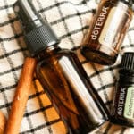 An amber spray bottle with cinnamon sticks and essential oils on a checkered towel.