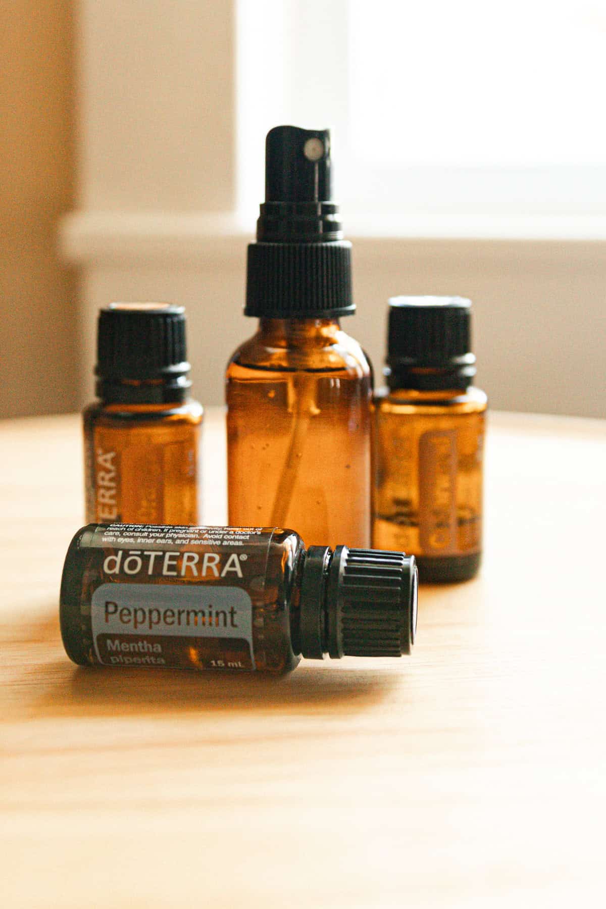 A glass spray bottle lined up with essential oil bottles on a wooden table. 