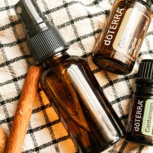 An amber spray bottle with cinnamon sticks and essential oils on a checkered towel.