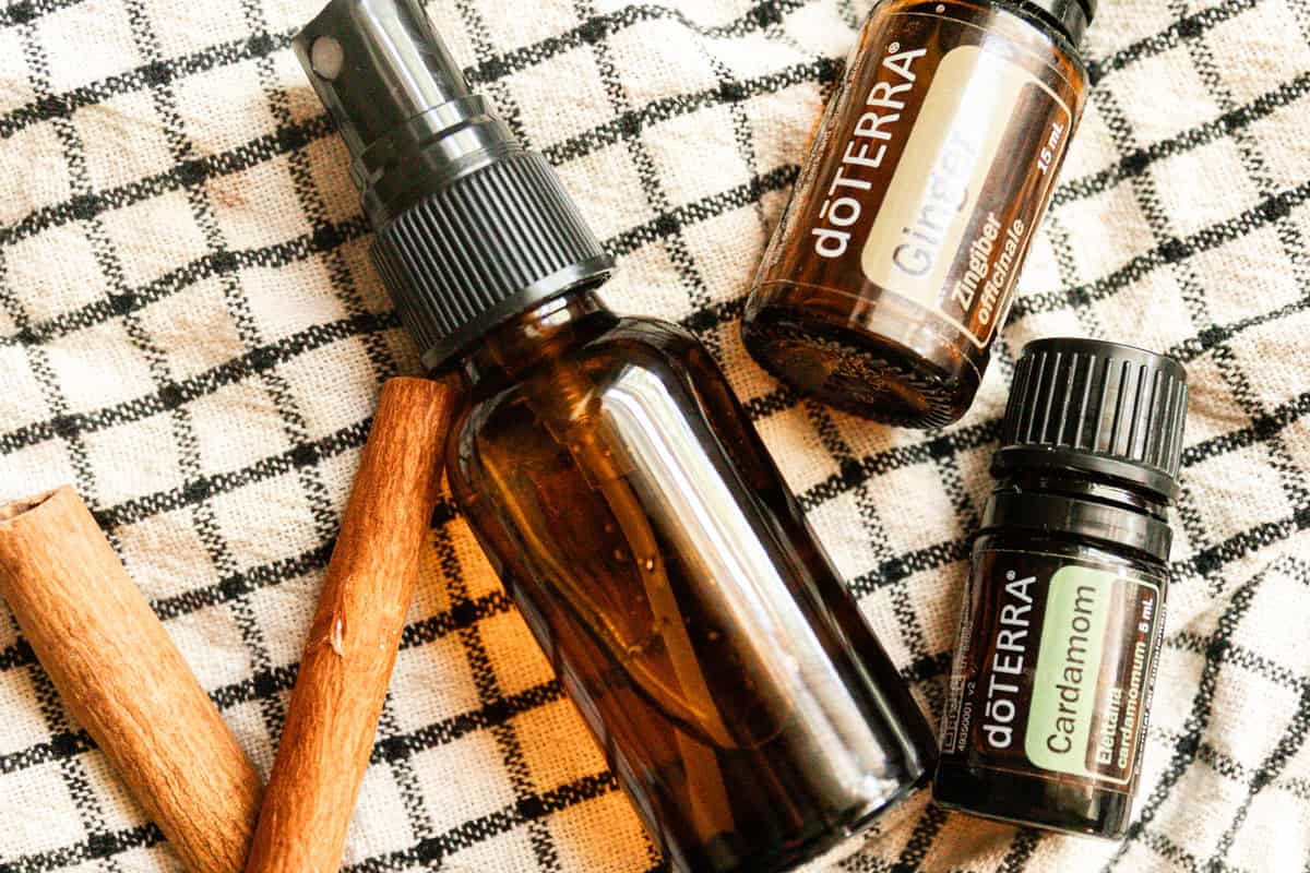 An amber spray bottle with cinnamon sticks and essential oils on a checkered towel. 