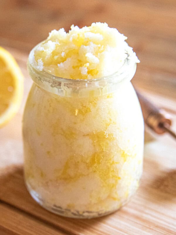 A jar of yellow hand scrub with a slice of lemon and a measuring spoon.