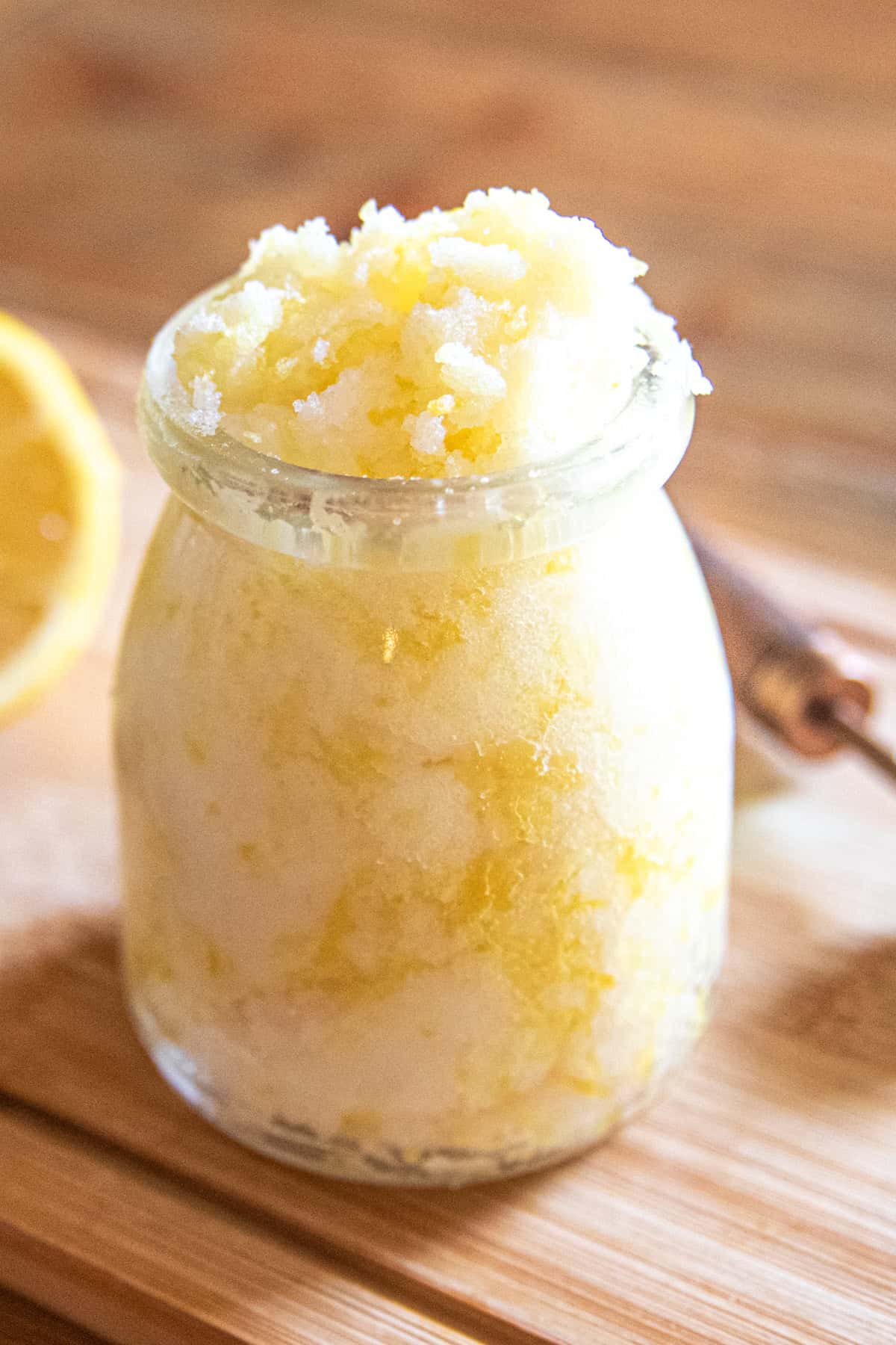 A jar of yellow hand scrub with a slice of lemon and a measuring spoon.