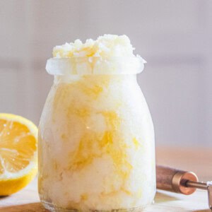 A jar of homemade hand scrub with a lemon half and a measuring spoon.