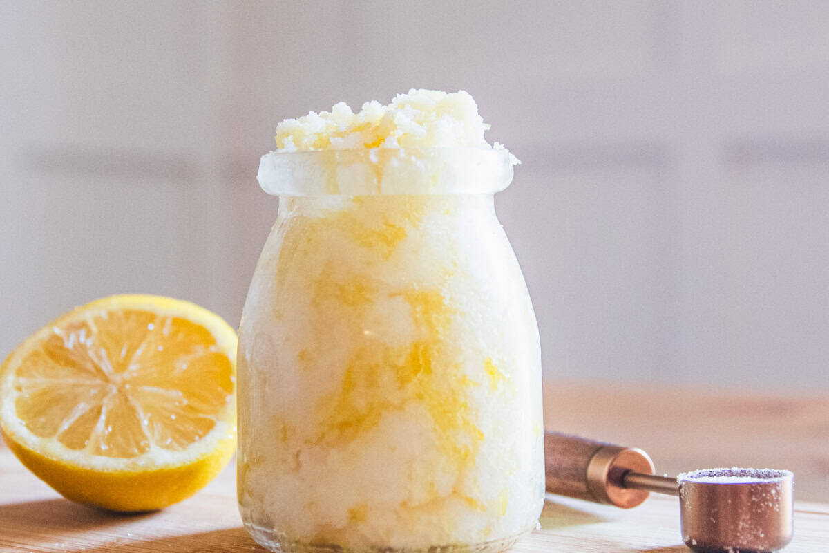 A jar of homemade hand scrub with a lemon half and a measuring spoon.