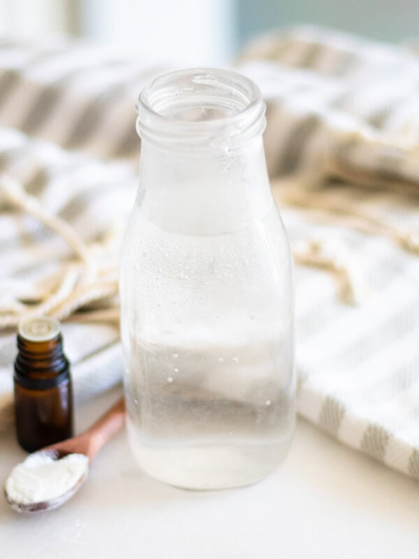 A bottle of homemade mouthwash with a bottle of essential oil and a spoonful of baking soda.