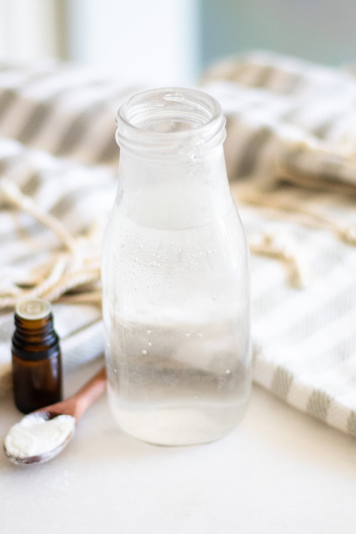 A bottle of homemade mouthwash with a bottle of essential oil and a spoonful of baking soda. 