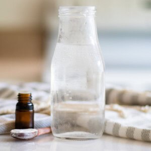 A jar of homemade mouthwash with a striped towel and a bottle of essential oil.