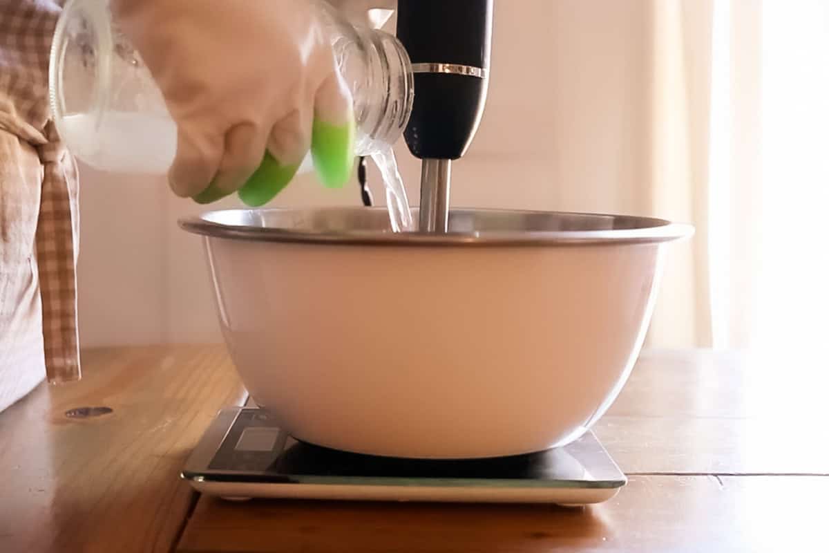 Pouring lye/water mixture into the mixing bowl while mixing with an immersion blender. 