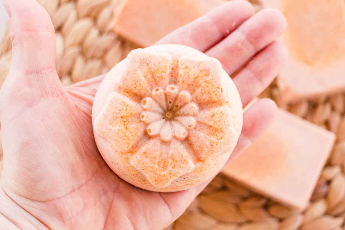 Holding a flower-shaped bar of orange soap in the palm of a hand.