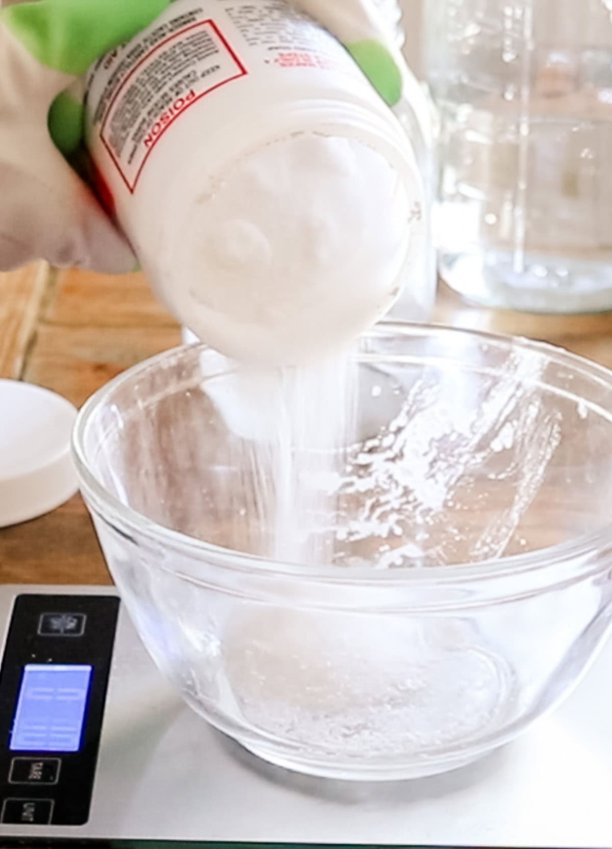 Pouring lye into a glass bowl on a digital scale.