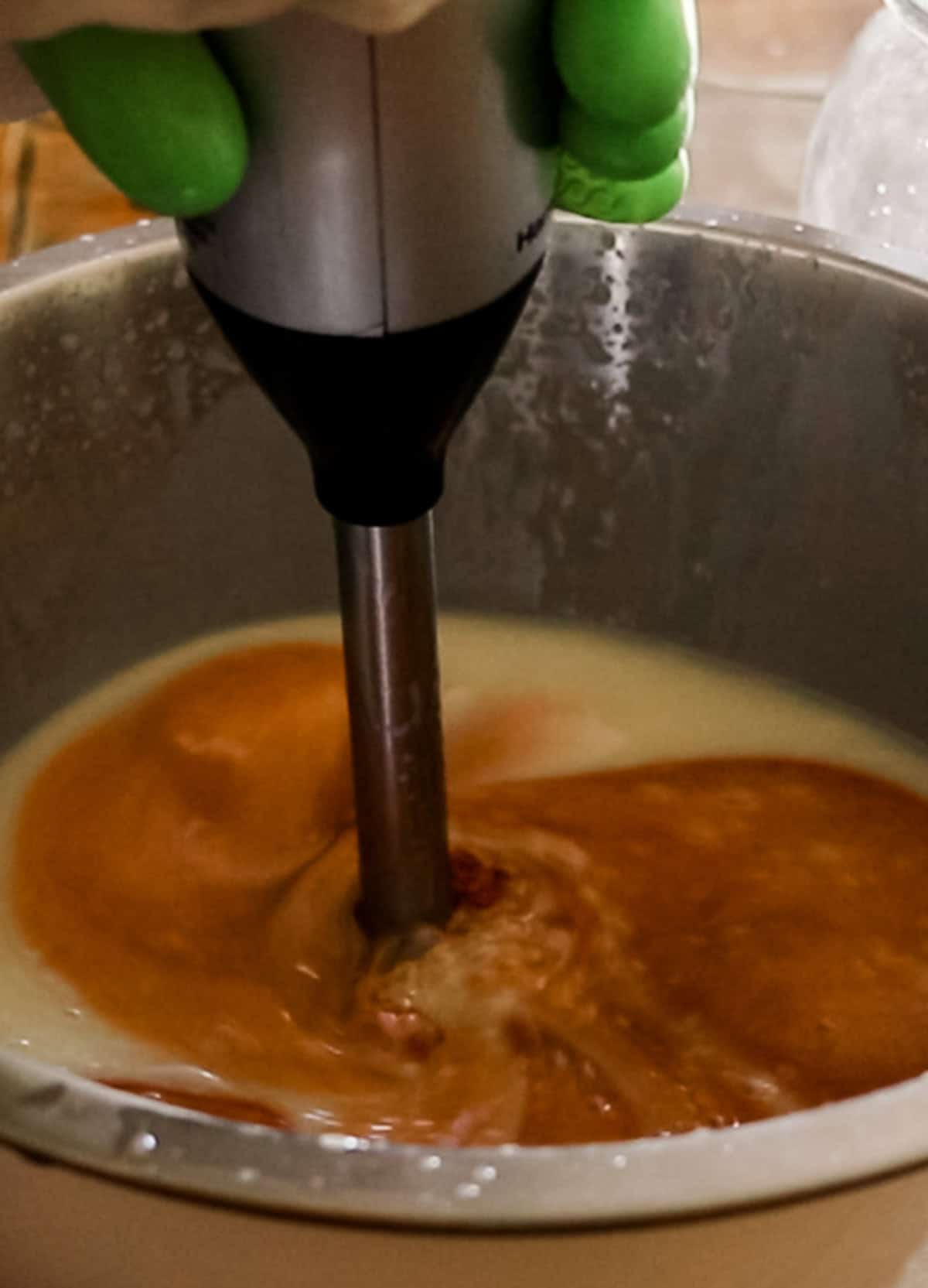Mixing turmeric into the soap ingredients with an immersion blender.