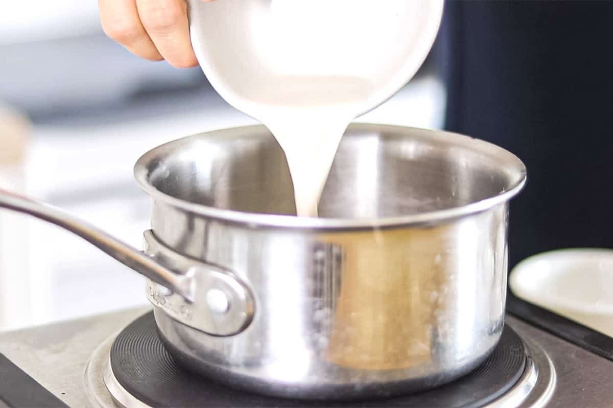 Pouring almond milk into a small saucepan.