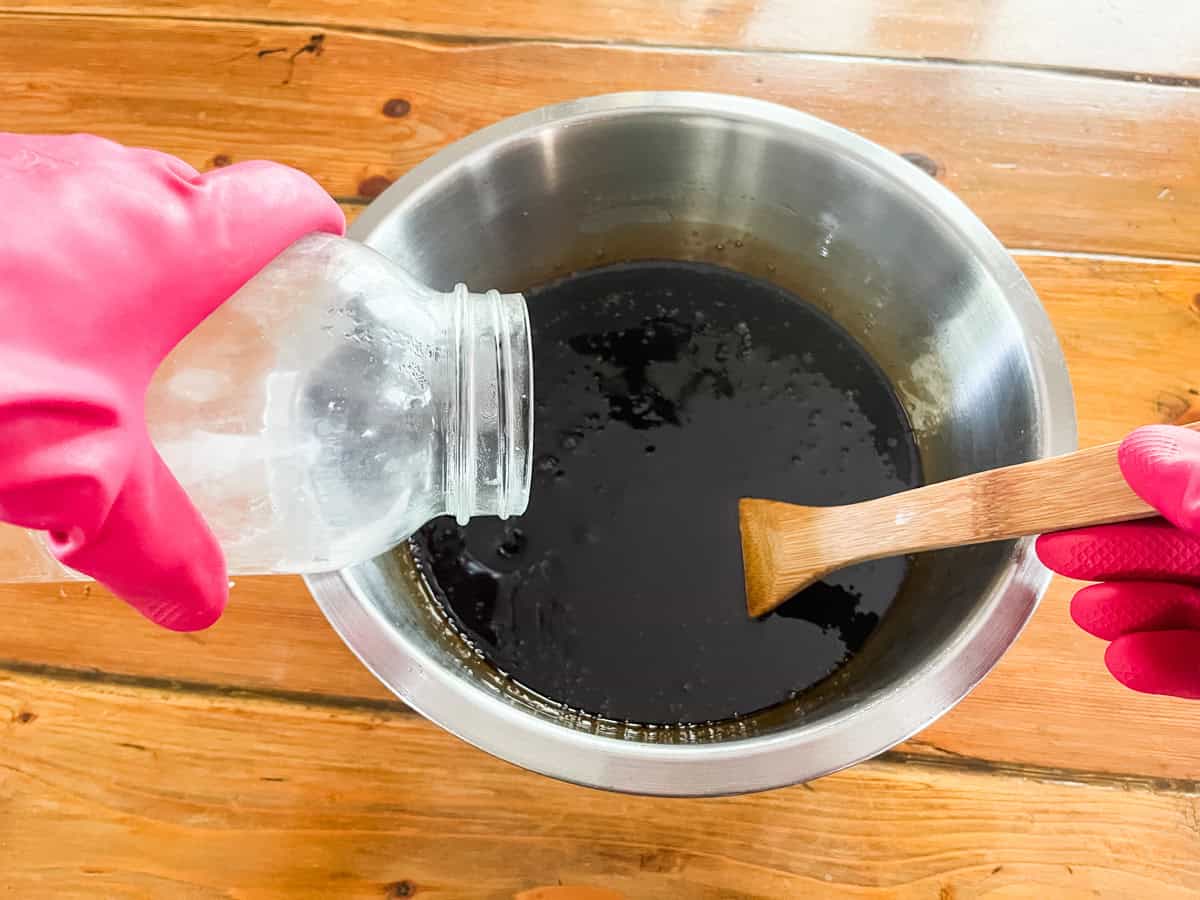 Pouring lye and water mixture into a bowl of oils and pine tar with a wooden spoon.