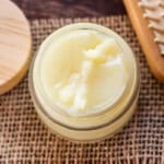 A jar of homemade hair pomade with a lid and a hairbrush next to it.