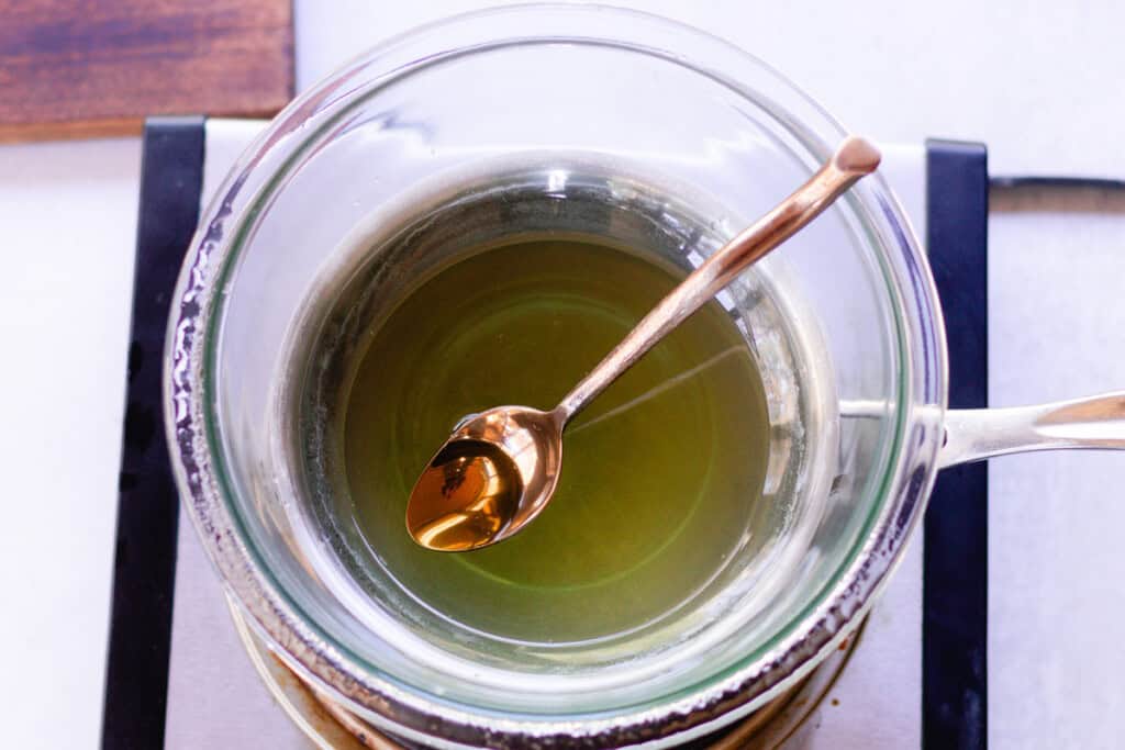 Melted hair pomade ingredients in a double boiler with a spoon.