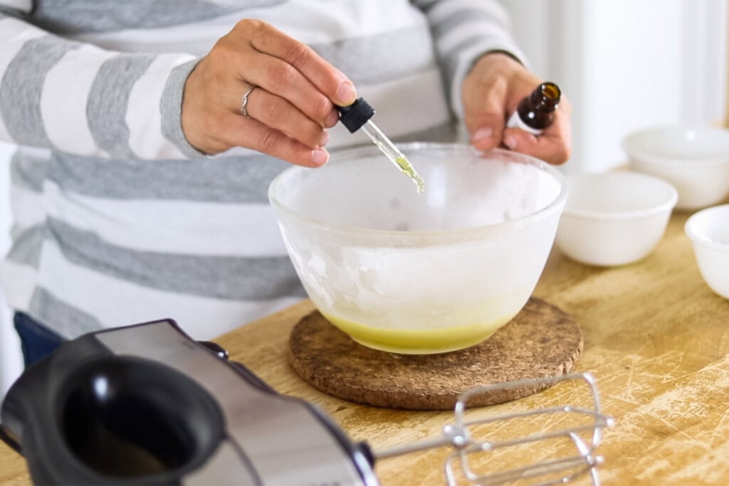 Adding vitamin E oil to a bowl of melted beard balm ingredients.