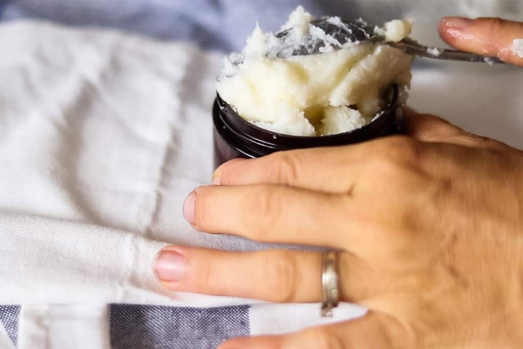 Scooping beard balm into a glass amber jar. 