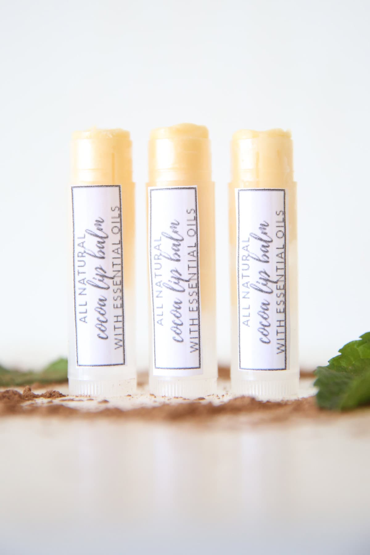 3 DIY lip balms in clear tubes with homemade labels on white marble.